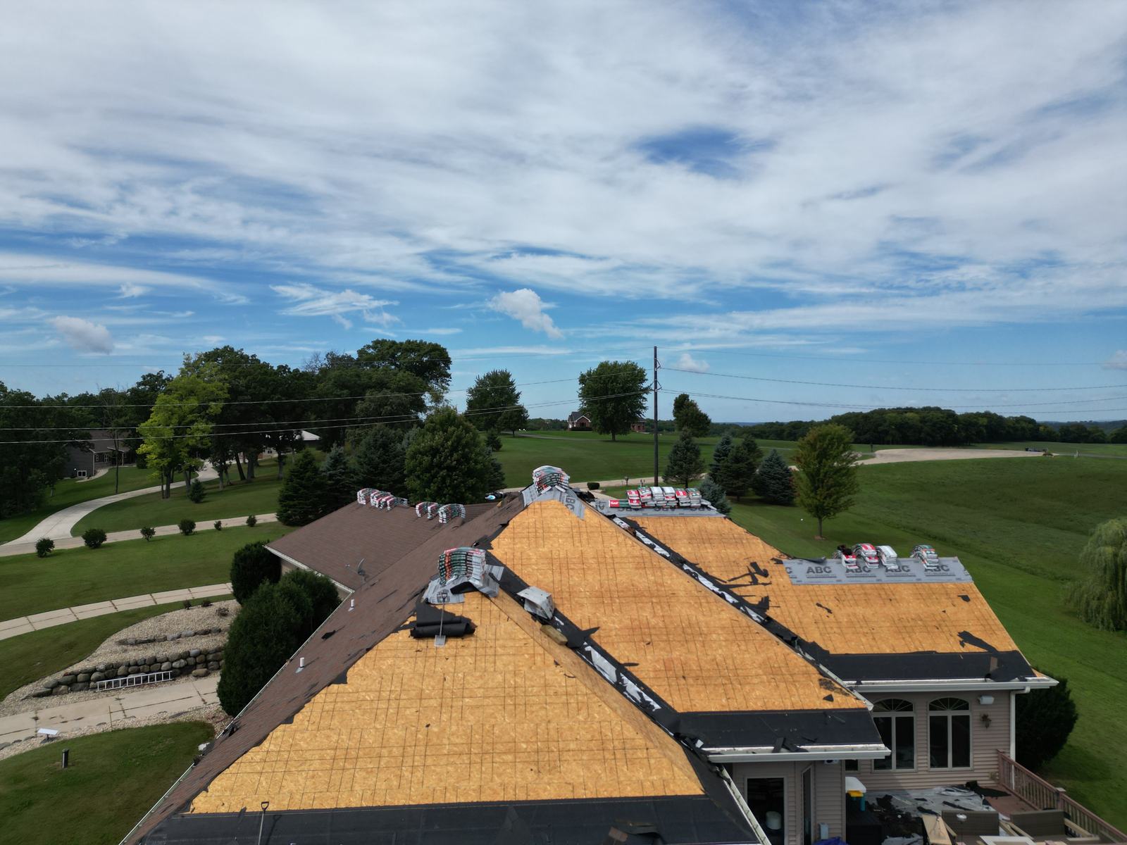 Drone view: roof decking exposed, underlayment and shingle bundles staged on the ridge