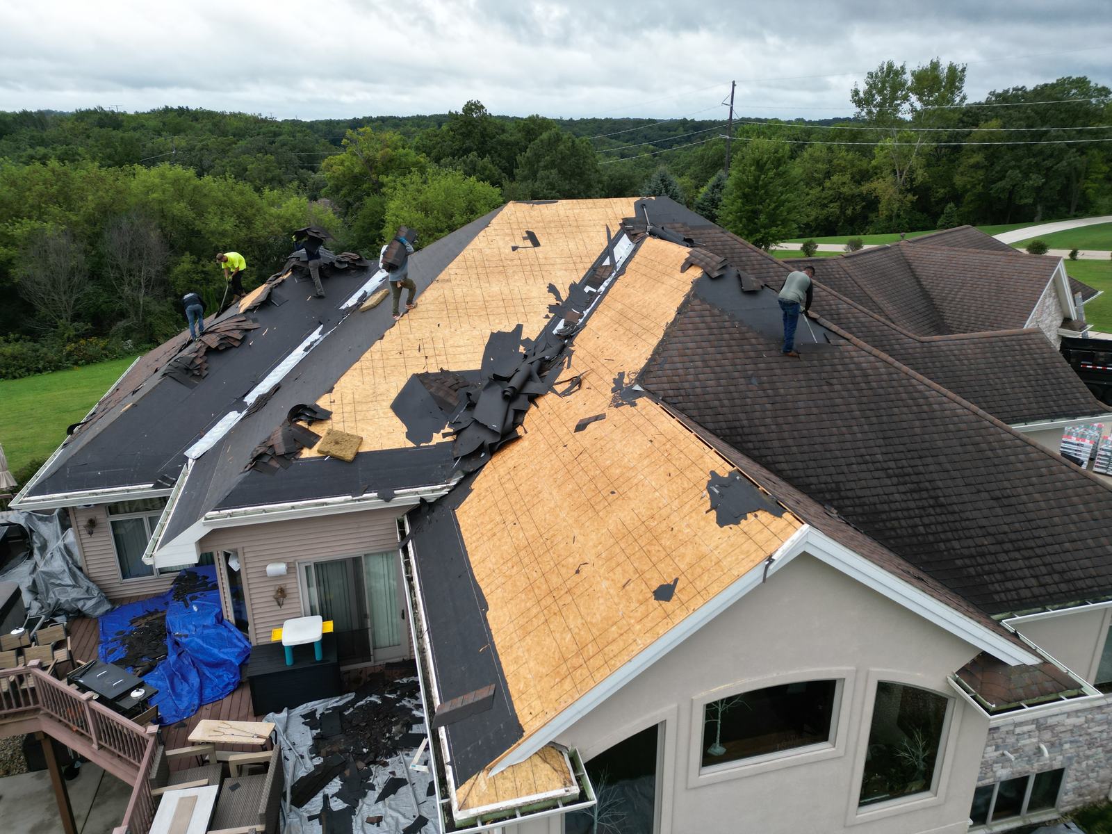 Drone view: crew tearing off the old shingle roof on a large stone home